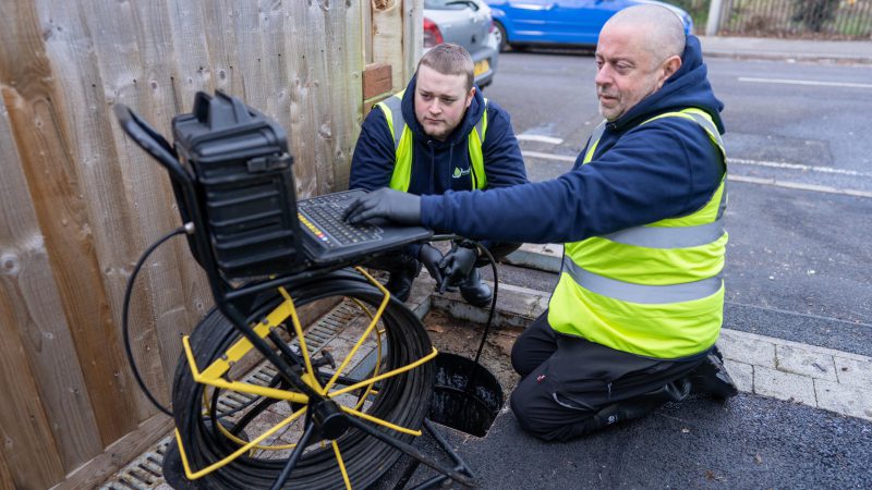 Drain engineer carrying out a CCTV drain survey at an inspection chamber with monitor, cable reel and survey paperwork showing CCTV drain survey cost UK guidance